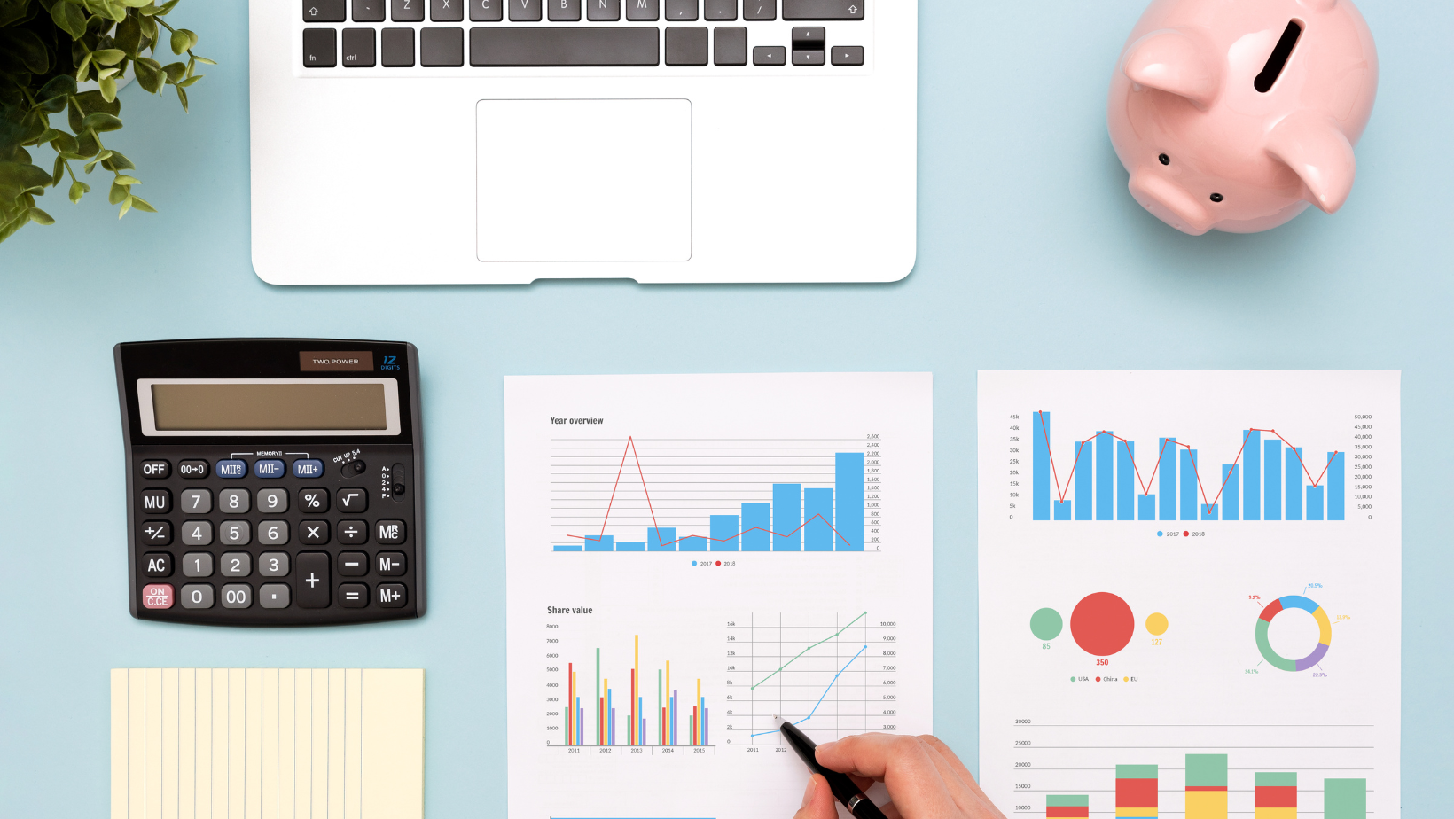 A blue desk with a laptop, calculator, piggy bank, and financial reports.