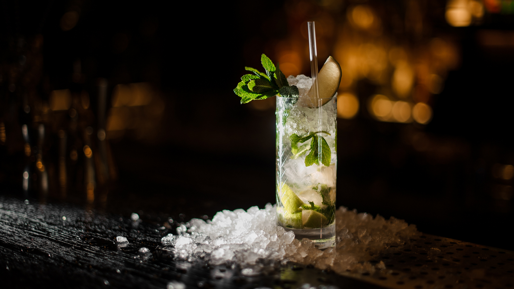 A freshly garnished cocktail with crushed ice, lime, and mint leaves against a darkly lit background.